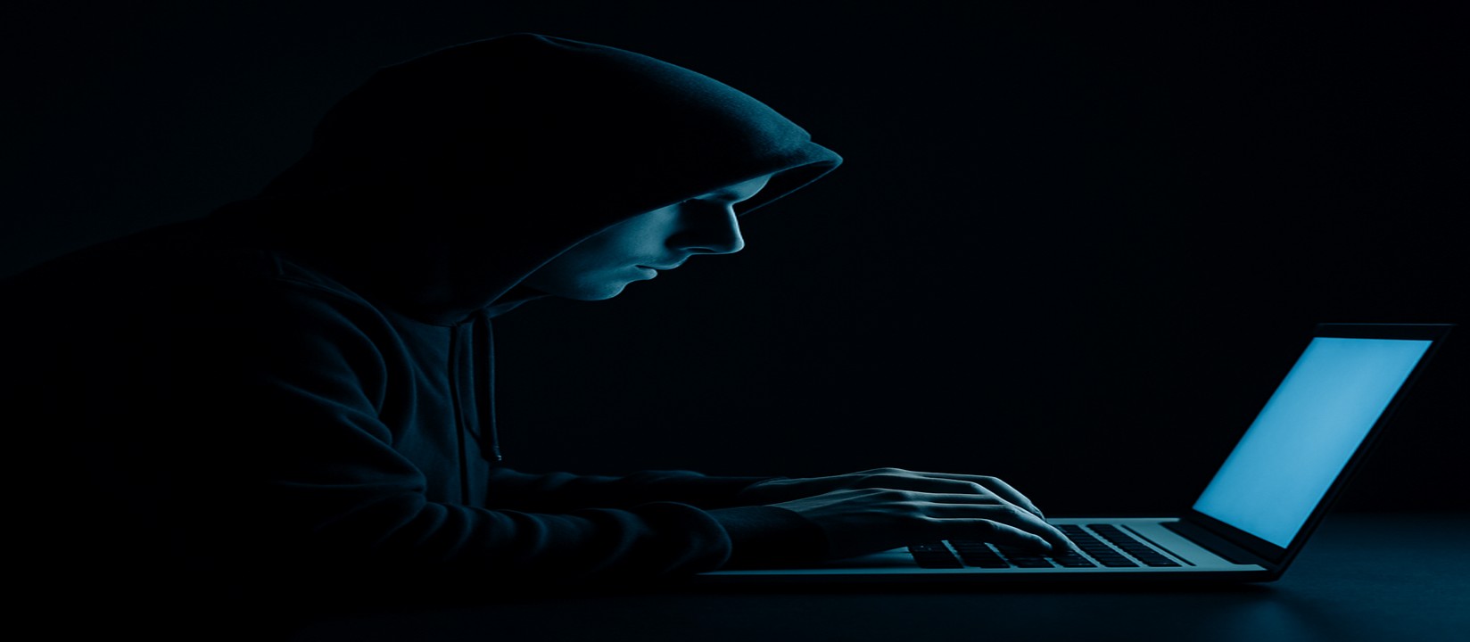 একজন ব্যক্তি অন্ধকার ঘরে ল্যাপটপে মনোযোগ দিয়ে 333bt ওয়েবসাইটে অনলাইন গেম খেলা করছেন